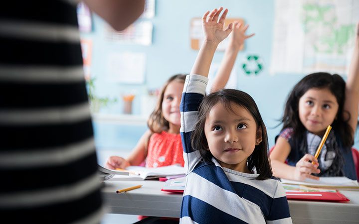 young children raising hands in school