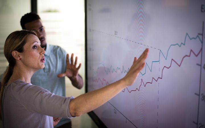 Two colleagues discussing data chart on a digital screen