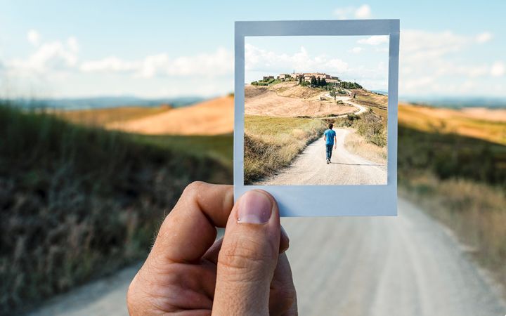 Hand holding up Polaroid picture of background scene 