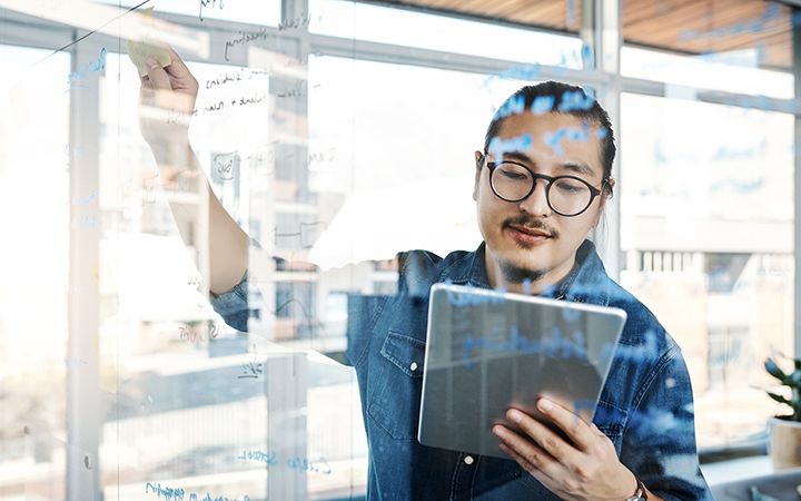 Man looking at tablet and posting sticky note on screen
